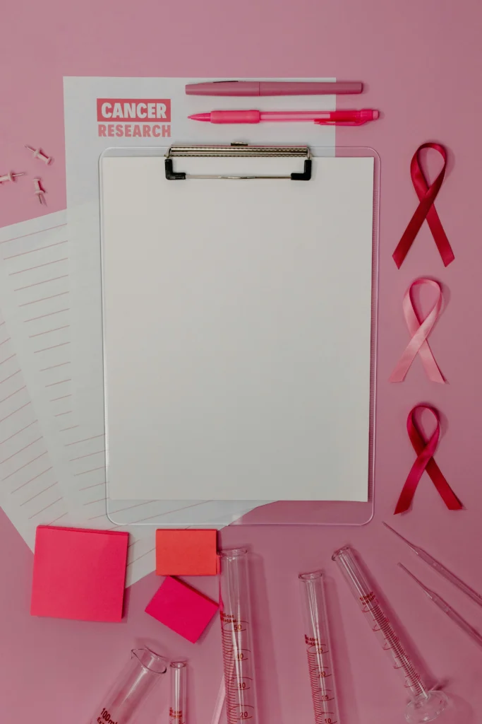 Clipboard with pink ribbons and cancer research papers on a pink background.