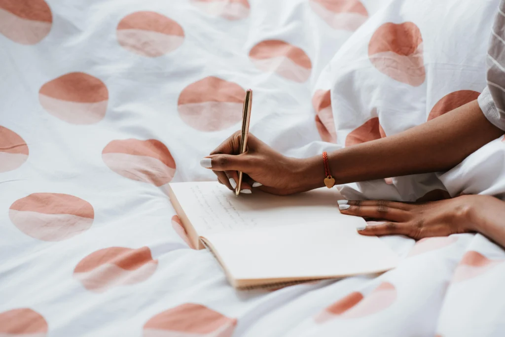A woman journaling on a bed with polka dot sheets, creating a cozy atmosphere.